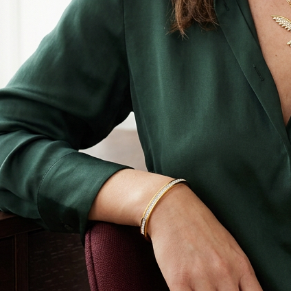 Elegant modellbild med fågelhalsband, guldarmband och mörkgrönt siden
