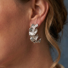 Mira Earrings Silver i närbild på örat med en lös hårlock och blå bakgrund