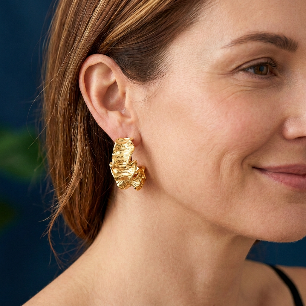 Mira Earrings Gold på modell med varma slingor och blå bakgrund