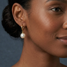 Liora Earrings Gold med rund imitationspärla i närbild på modell mot blå bakgrund