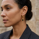 Aira Noir Earrings Gold buret på modell med bakåtstruket hår och mörk kavaj